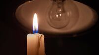 Burning candle near a switched off light bulb in complete darkness.