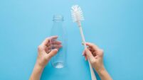 Young adult woman hands holding white brush and transparent plastic bottle on light blue table background. Pastel color. Point o
