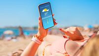 Woman sunbathing on the beach in hot summer day and checking weather forecast on mobile phone.