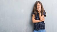 Young hispanic kid over grunge grey wall looking stressed and nervous with hands on mouth biting nails. Anxiety problem.