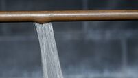 A close-up of a ruptured copper pipe spraying water against a basement wall