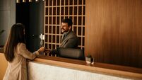 Smiling receptionist behind the hotel counter attending to a female guest. The concierge gives the documents to hotel guest.