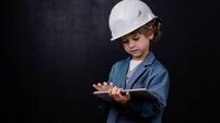 Serious cute little boy in hardhat and formalwear using digital tablet