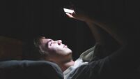 Depressed teenager on his phone in the dark.