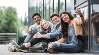 happy friends smiling, sitting and taking selfie with smartphone