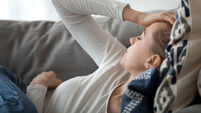 Upset depressed young woman lying on couch feeling strong headache
