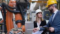 Chief engineer and project manager in modern industrial factory with robot arms talking and planning optimization of production.