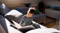 Caucasian toddler boy reading a child book, while sitting on a sofa in pajamas.