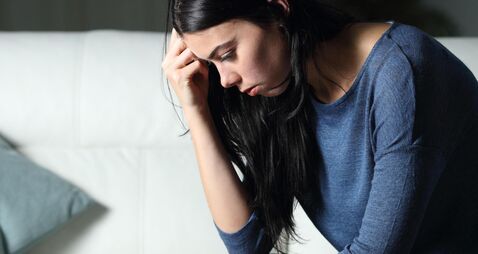 Worried woman thinking alone sitting on a couch in the night at home