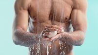 Muscular, shower and man with soap, water and cleaning himself with blue studio background, hygiene or wellness. Hands, male or