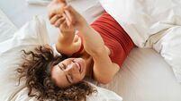 Happy smiling woman stretching on bed in the morning