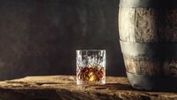 Glass of whisky or bourbon in ornamental glass next to a vinatge wooden barrel on a rustic wood and dark background