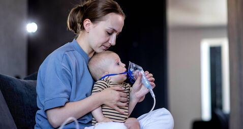 Mom giving nebulizer breathing treatment to sick infant baby at home