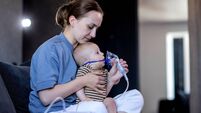 Mom giving nebulizer breathing treatment to sick infant baby at home