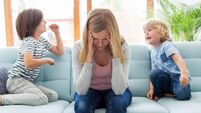 Mother with headache and children jumping on sofa